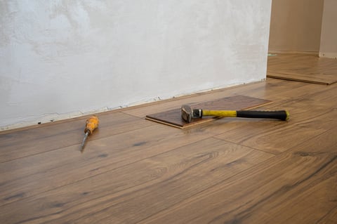 Laminate flooring is being laid down using a hammer and screwdriver on a wooden subfloor