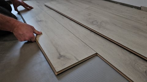 Worker laying wooden flooring boards during installation