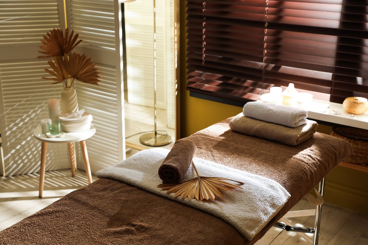 Massage table with supplies near window in stylish spa center. Interior design