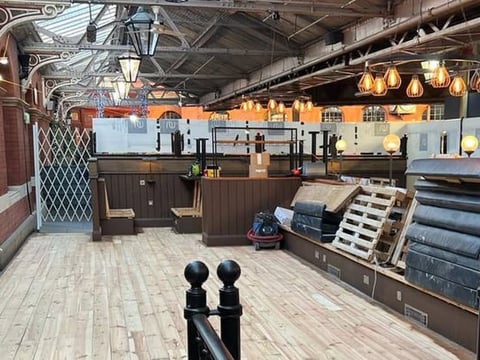 Interior of modern industrial loft space with kitchen appliances, pendant lighting, exposed ceiling, and polished wood flooring
