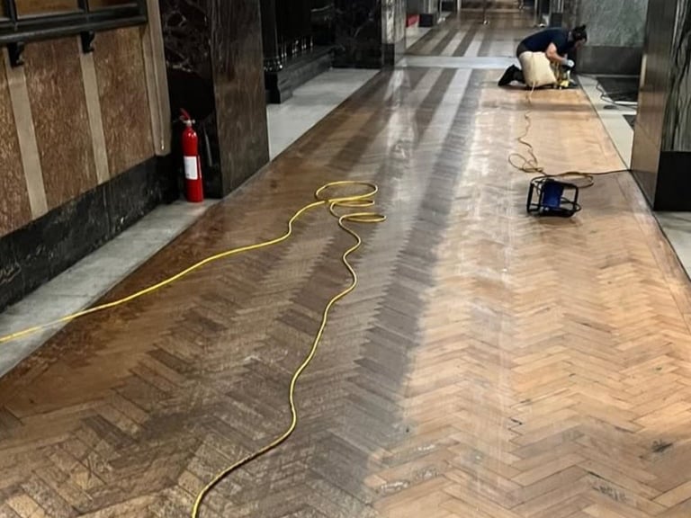 Indoor hallway with herringbone wood flooring partially cleaned, yellow equipment cord, and restoration work in progress