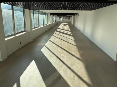 Long empty corridor with polished concrete floor, large windows along left side letting in natural light, and exposed ceiling structure