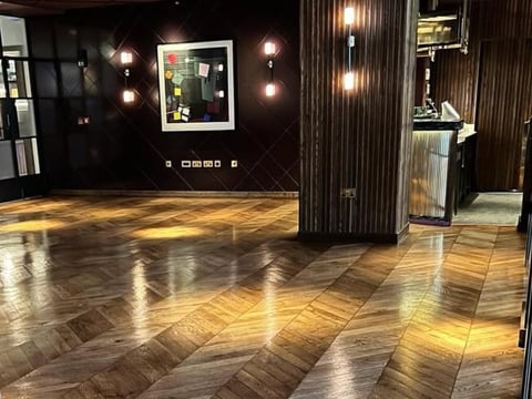 Modern lobby with herringbone wood flooring, dark walls, framed artwork, and hanging pendant lights
