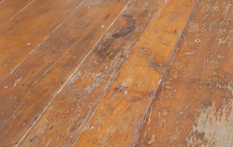 Close-up of worn hardwood floor with diagonal planks showing scratches and weathering