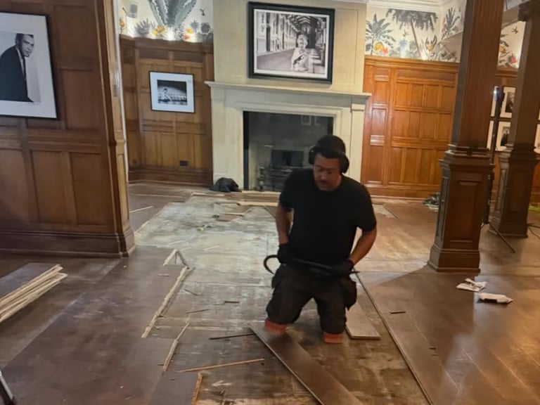 Person in black clothing working on floor installation in elegant wooden-paneled interior space with fireplace