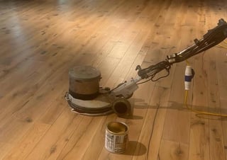 Floor buffer machine on wooden flooring with cleaning supplies nearby