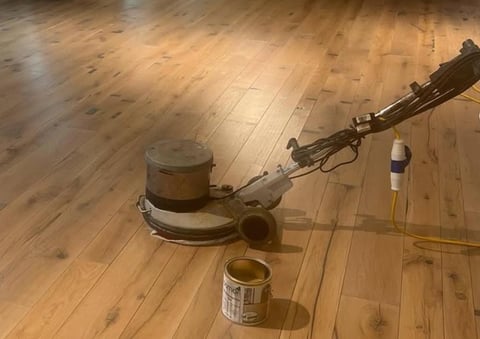 Floor buffer machine on wooden flooring with cleaning supplies nearby