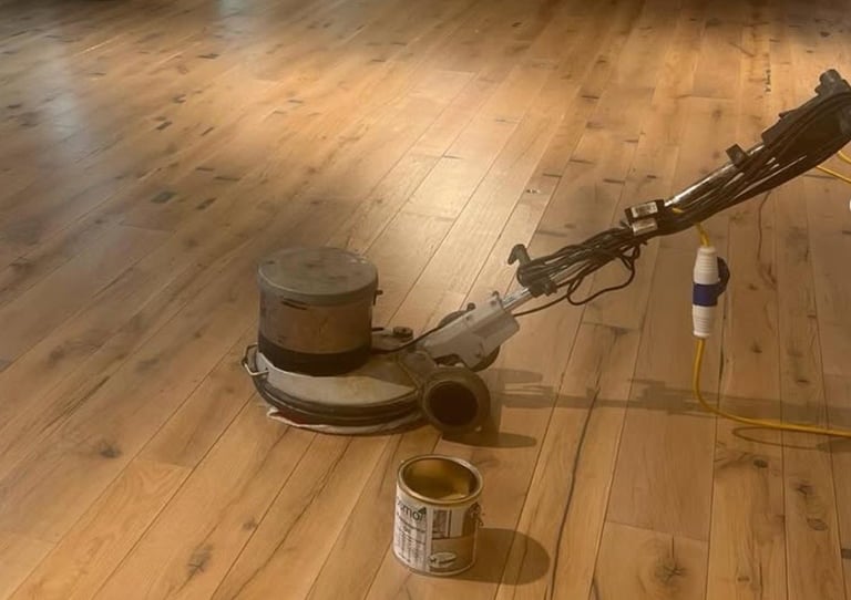 Floor buffer machine on wooden flooring with cleaning supplies nearby