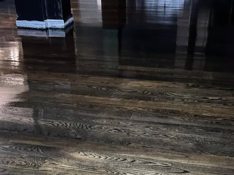 Dark wood-grain flooring with wet reflective surface and columns in a modern interior space