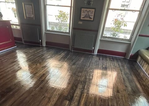 Empty room with dark wood flooring, large windows with natural light, and burgundy wall trim along the base