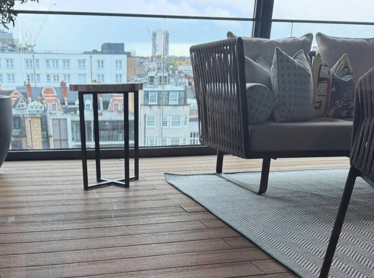 Modern rooftop lounge with wooden deck, black minimalist furniture, and panoramic city skyline views through floor-to-ceiling windows