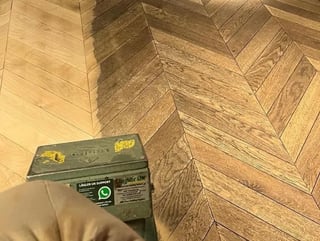 A hand holding a green Stanley level tool on a herringbone wood floor pattern