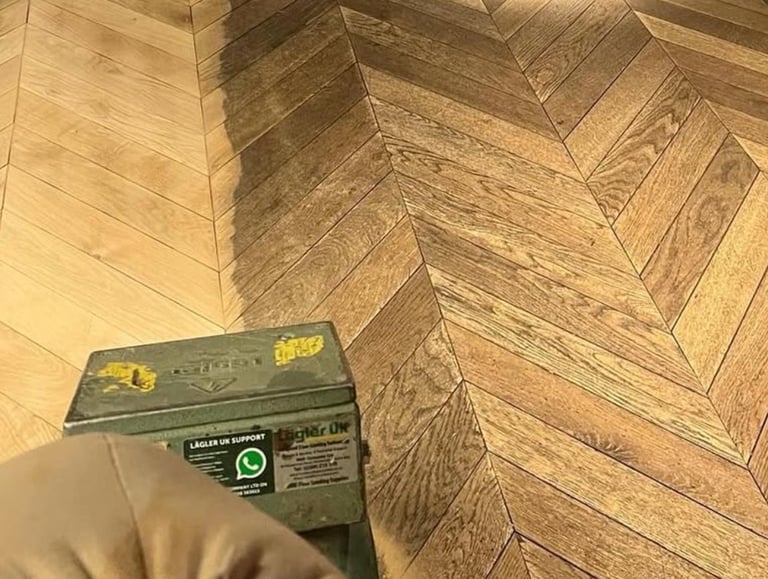 A hand holding a green Stanley level tool on a herringbone wood floor pattern