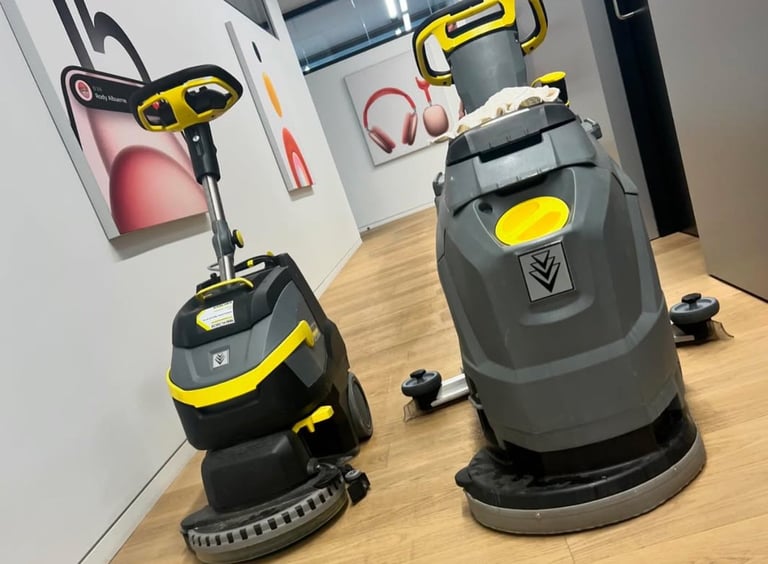 Two commercial floor cleaning machines with yellow and black detailing displayed on wooden flooring in a showroom setting.