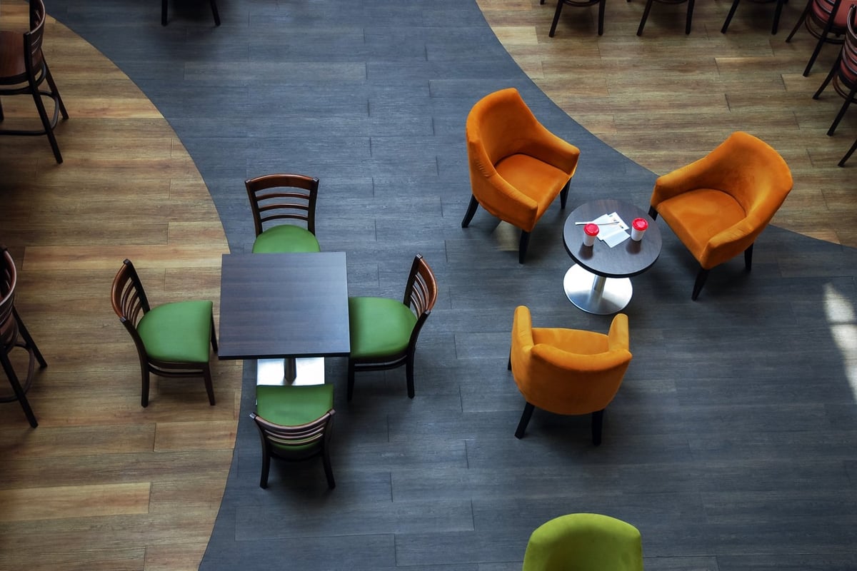 Overhead view of modern office lounge with green chairs at square table and orange armchairs around circular table on blue flooring