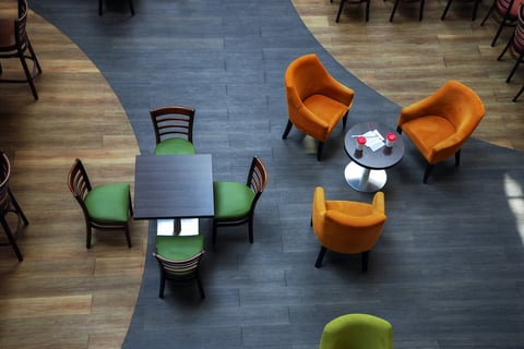 Overhead view of modern office lounge with green chairs at square table and orange armchairs around circular table on blue flooring