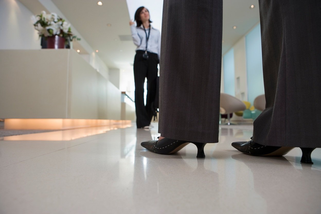 Professional woman in business attire walking through modern office lobby with polished floors and contemporary decor