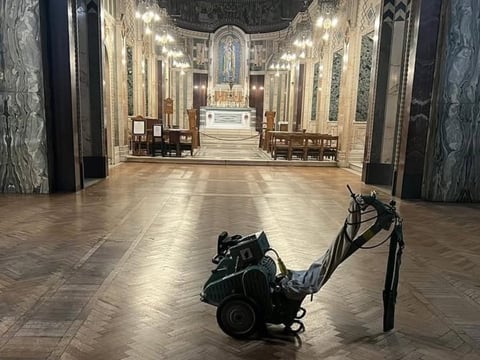 Black motorcycle parked in center aisle of ornate church with marble columns, altar, and wooden pews