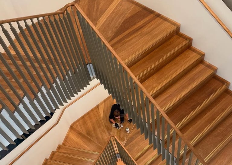 Overhead view of wooden spiral staircase with metal railing and person standing on landing below