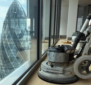 Commercial floor polishing machine on wooden floor next to large windows overlooking modern glass building