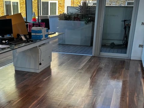 Modern open office space with wooden flooring, desk workspace, planters, and glass doors leading to outdoor patio area