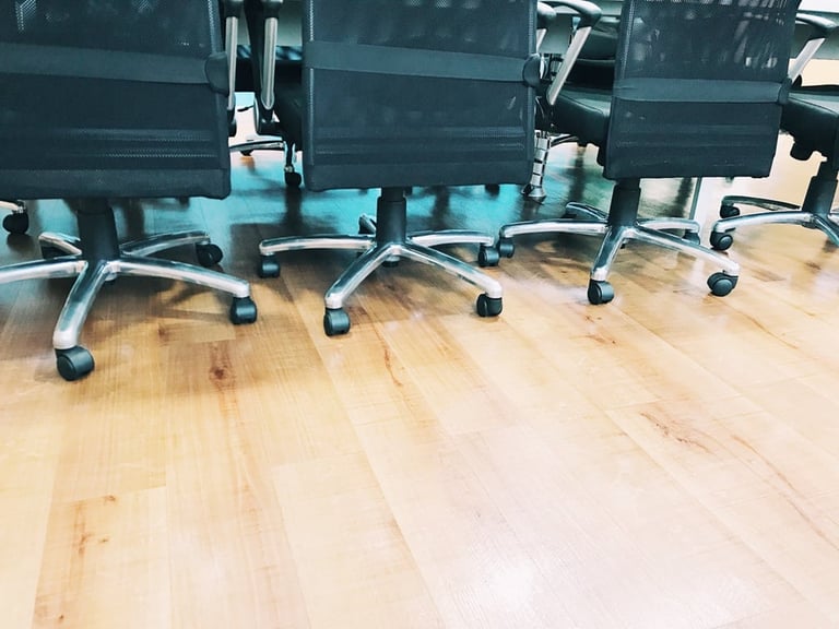 Row of four blue office chairs with casters lined up on a light wooden floor