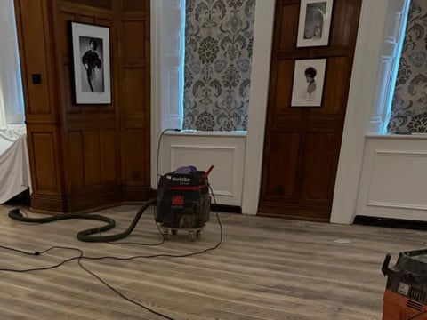 Interior room with wooden doors, wood-look flooring, and cleaning equipment including a black wet/dry vacuum and red machine connected by cords