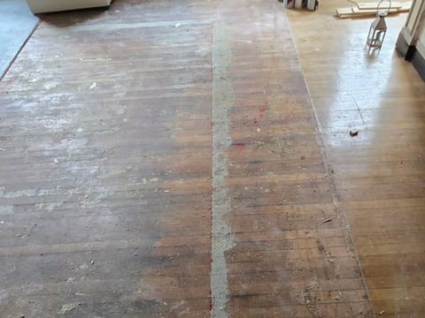 Hardwood floor with tape marking sections, showing wear and dust