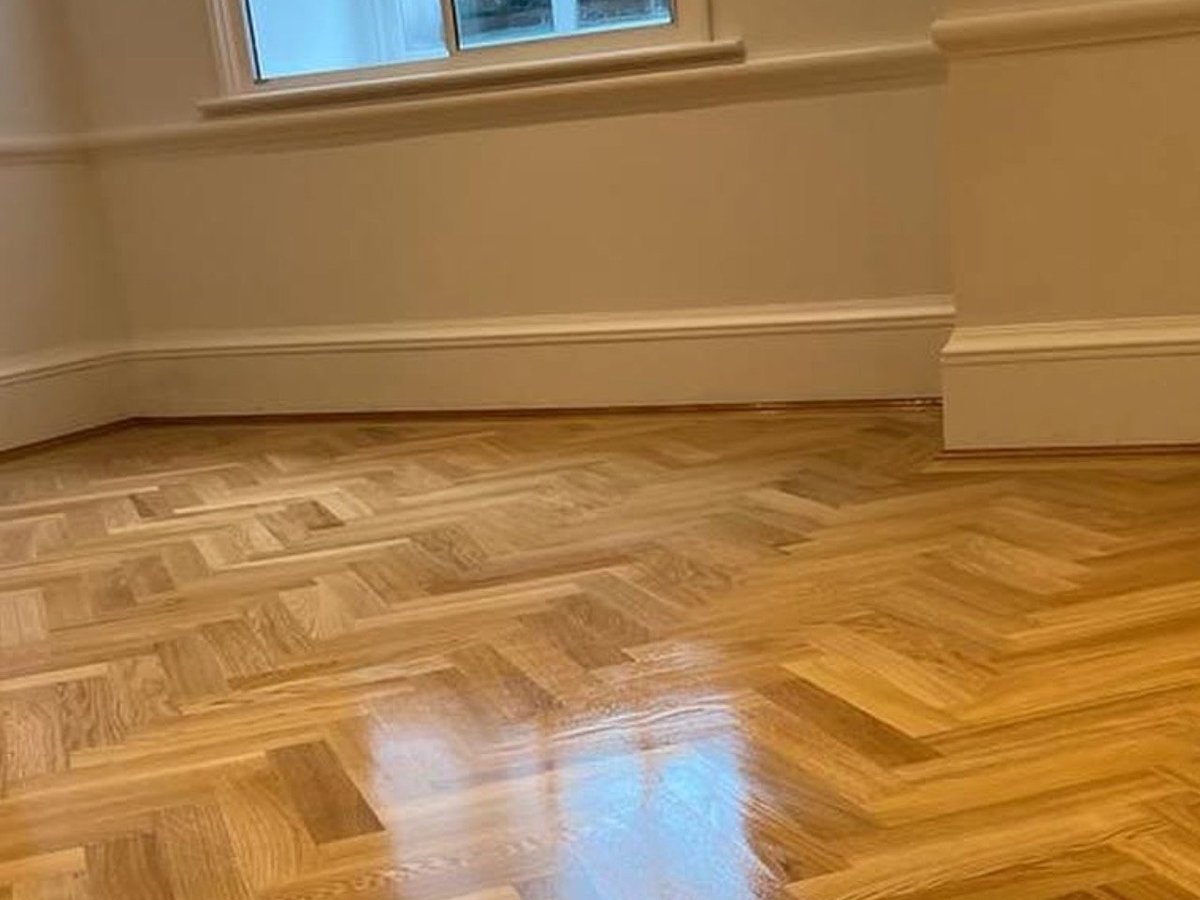 Empty room with cream walls, herringbone hardwood floors, baseboards, and a window with natural light